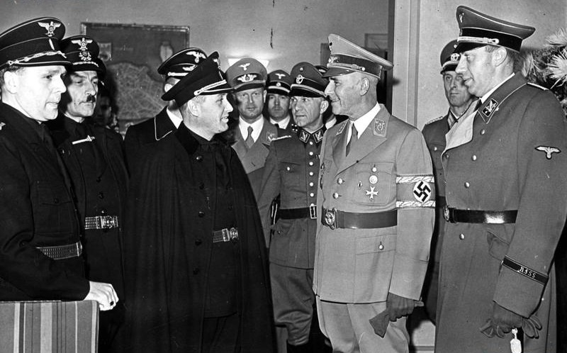 Slovenský minister vnútra Alexander Mach (tretí zľava) a nemecký ríšsky minister vnútra Wilhelm Frick (druhý sprava) počas stretnutia v októbri 1942 (Zdroj: Narodowe Archiwum Cyfrowe, archívne označenie 2-12461, Wikimedia Commons).